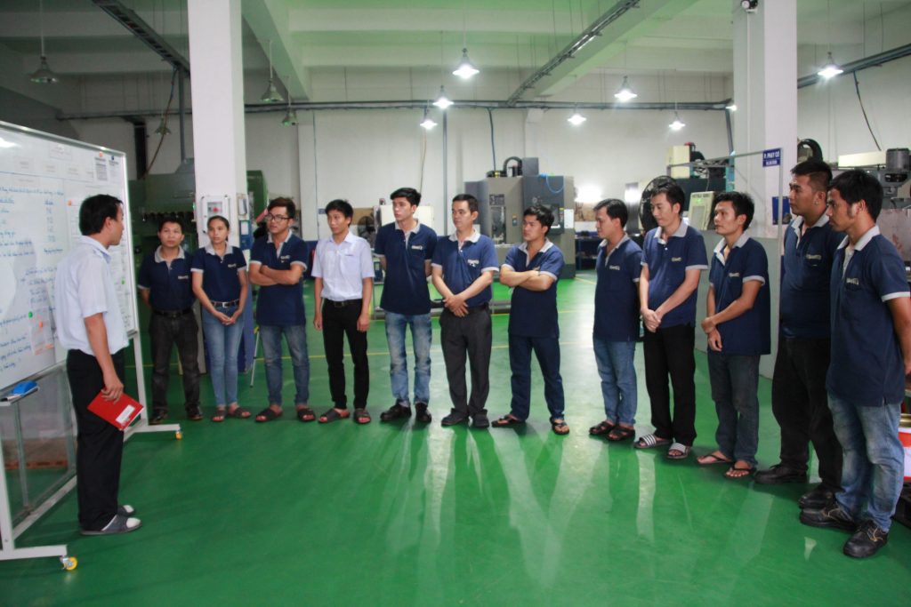 工場で前に立っている男性がほかのメンバーに指導している